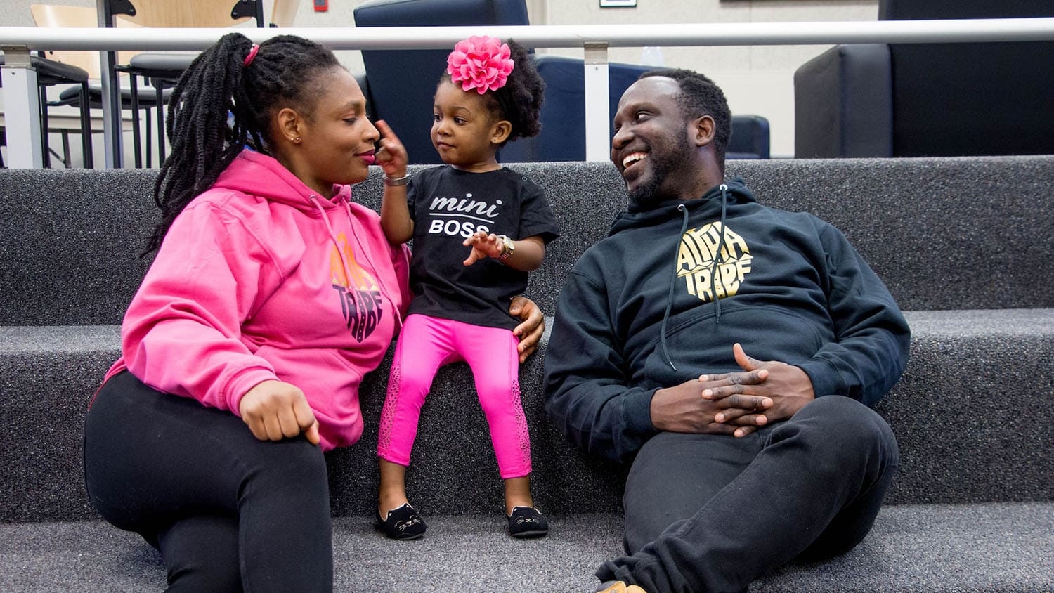 a Black man and woman sit on either side of a playful Black toddler